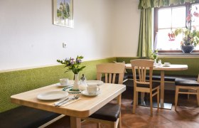 Gemütlicher Frühstücksraum mit Holztischen, grünen Bänken und Blumen auf dem Tisch.