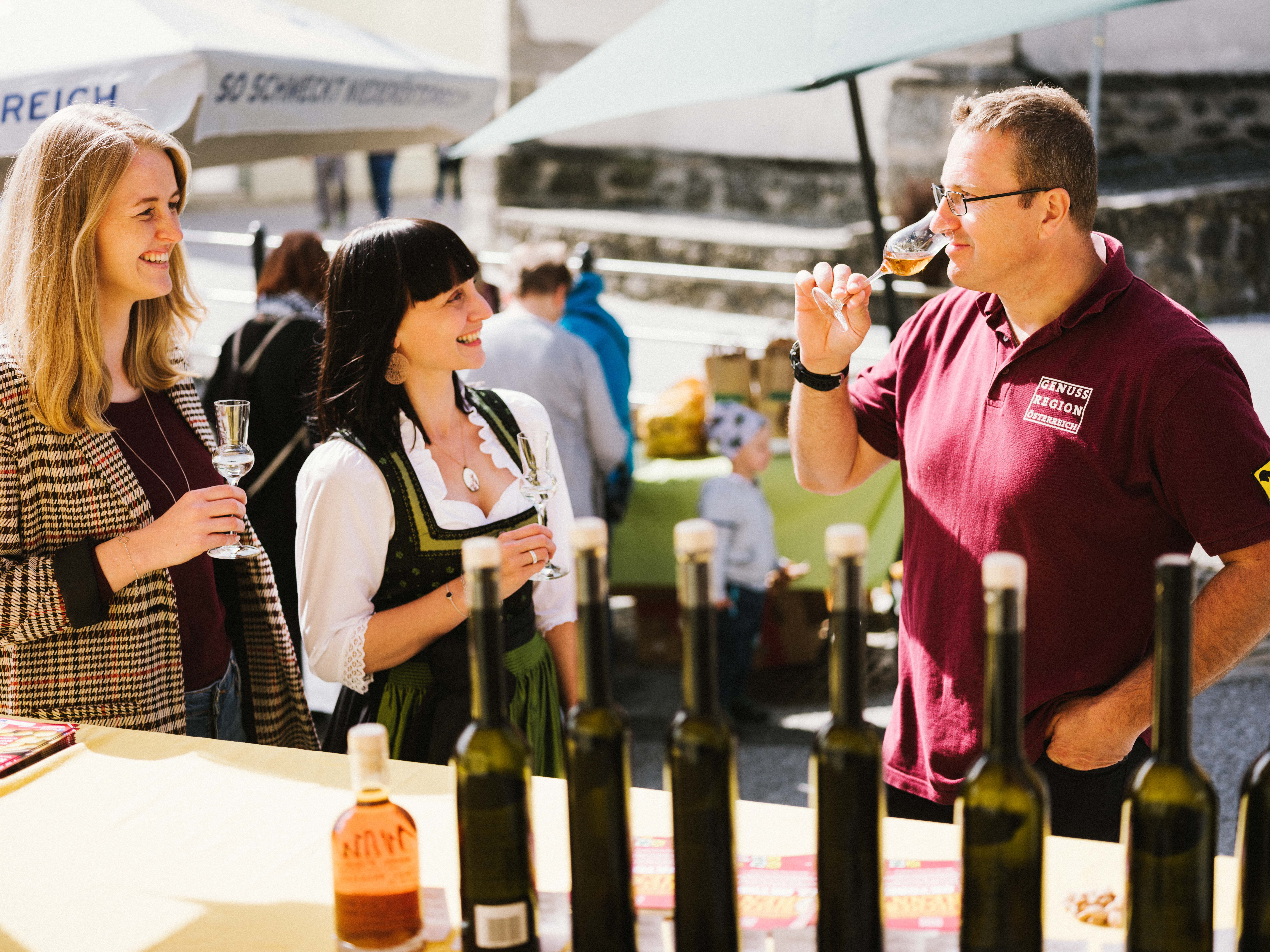 Drei Personen bei einer Schnapsverkostung auf einem Markt.