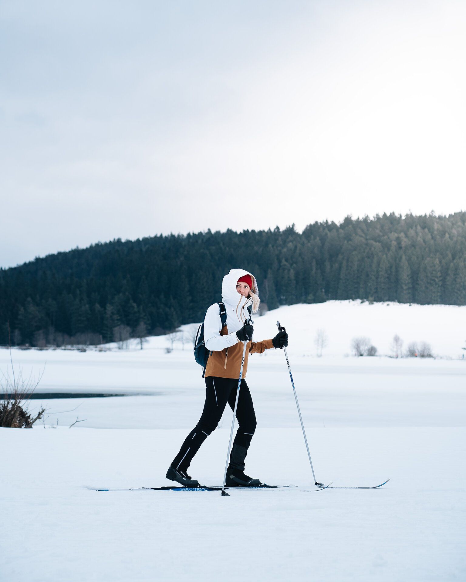 Eine Person beim Skilanglauf auf einem verschneiten Feld vor einem Wald.