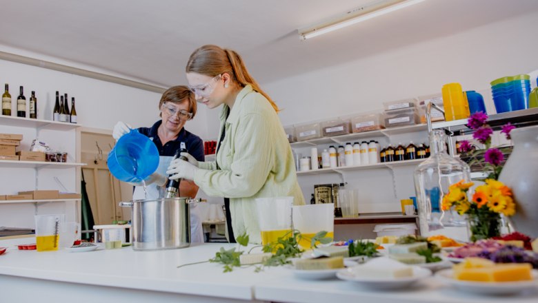 Zwei Personen stellen in einer Werkstatt Seife her, umgeben von Zutaten und Werkzeugen.