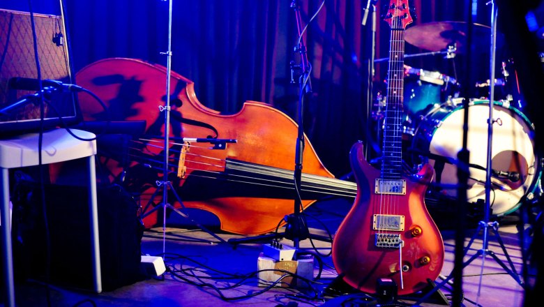 Musikinstrumente auf einer Bühne, darunter eine Gitarre, ein Kontrabass und ein Schlagzeug.