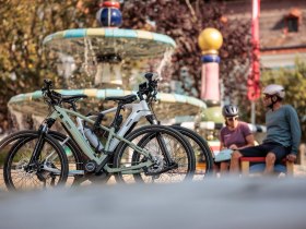 In der warmen Sonne entspannen Radfahrer am Hundertwasserbrunnen, umgeben von sprudelndem Wasser und bunten Pflanzen. Die frische Luft und die malerische Kulisse laden dazu ein, die Sch&ouml;nheit der Natur zu genie&szlig;en und neue Energie zu tanken.