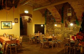 Gemütlicher Gastraum mit Holztischen und Stühlen, dekoriert mit Blumen und Bildern an den Wänden.