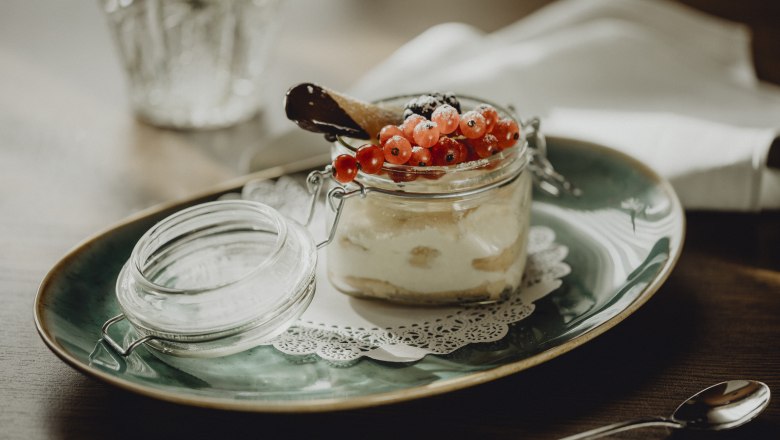 Dessert im Glas mit roten Johannisbeeren und Schokoladenkeks auf grünem Teller.