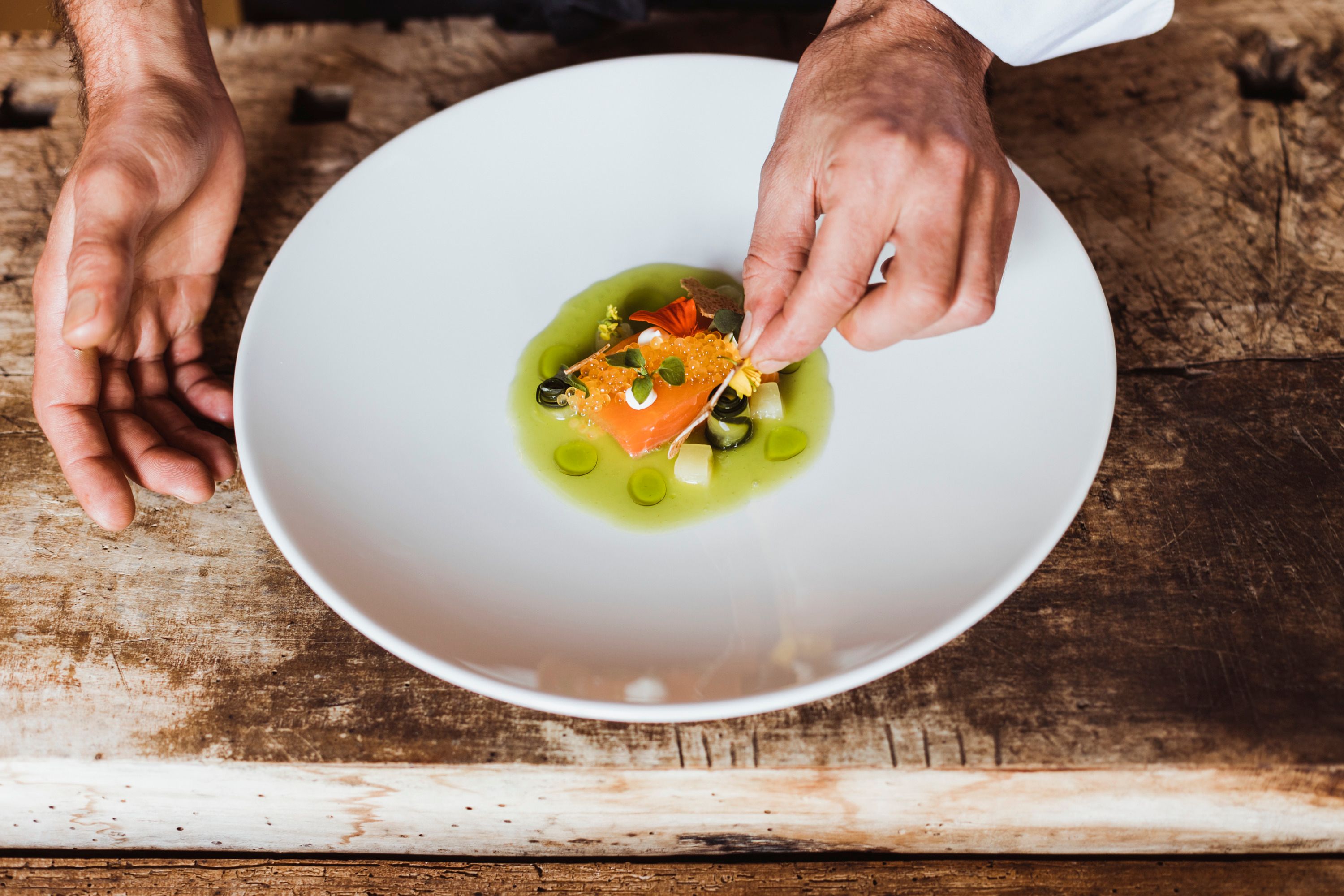 Ein Teller mit mariniertem Fisch und Kaviar, dekoriert mit grüner Sauce und Kräutern.