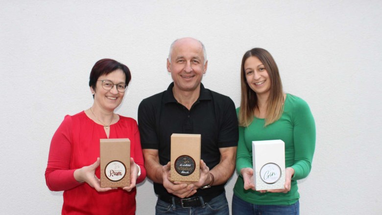 Drei Personen halten Geschenkboxen mit Rum, Whiskey und Gin vor einer weißen Wand.