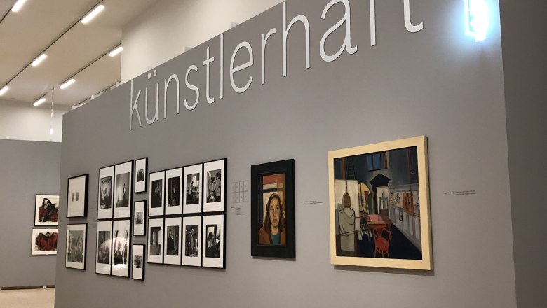 Ausstellungswand mit Kunstwerken und dem Schriftzug 'k&uuml;nstlerhaft'.