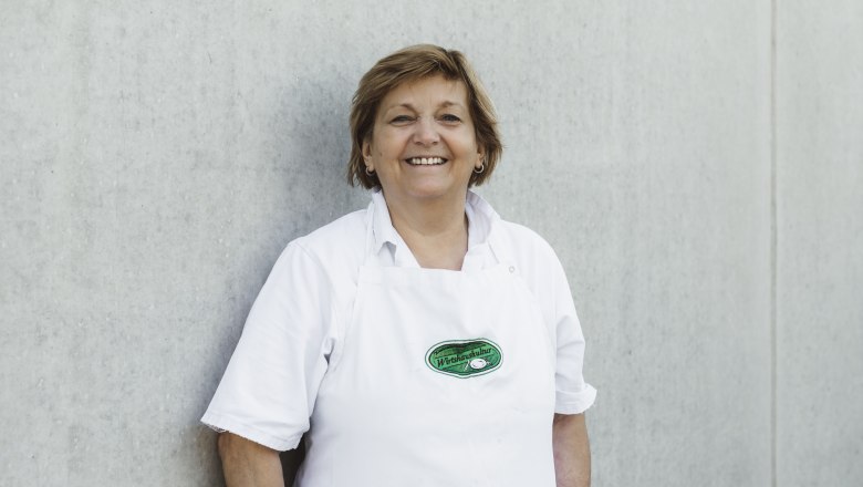 Frau in weißer Schürze vor grauer Wand.