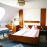 Comfortable hotel room with double bed, wooden furniture and table with chairs.