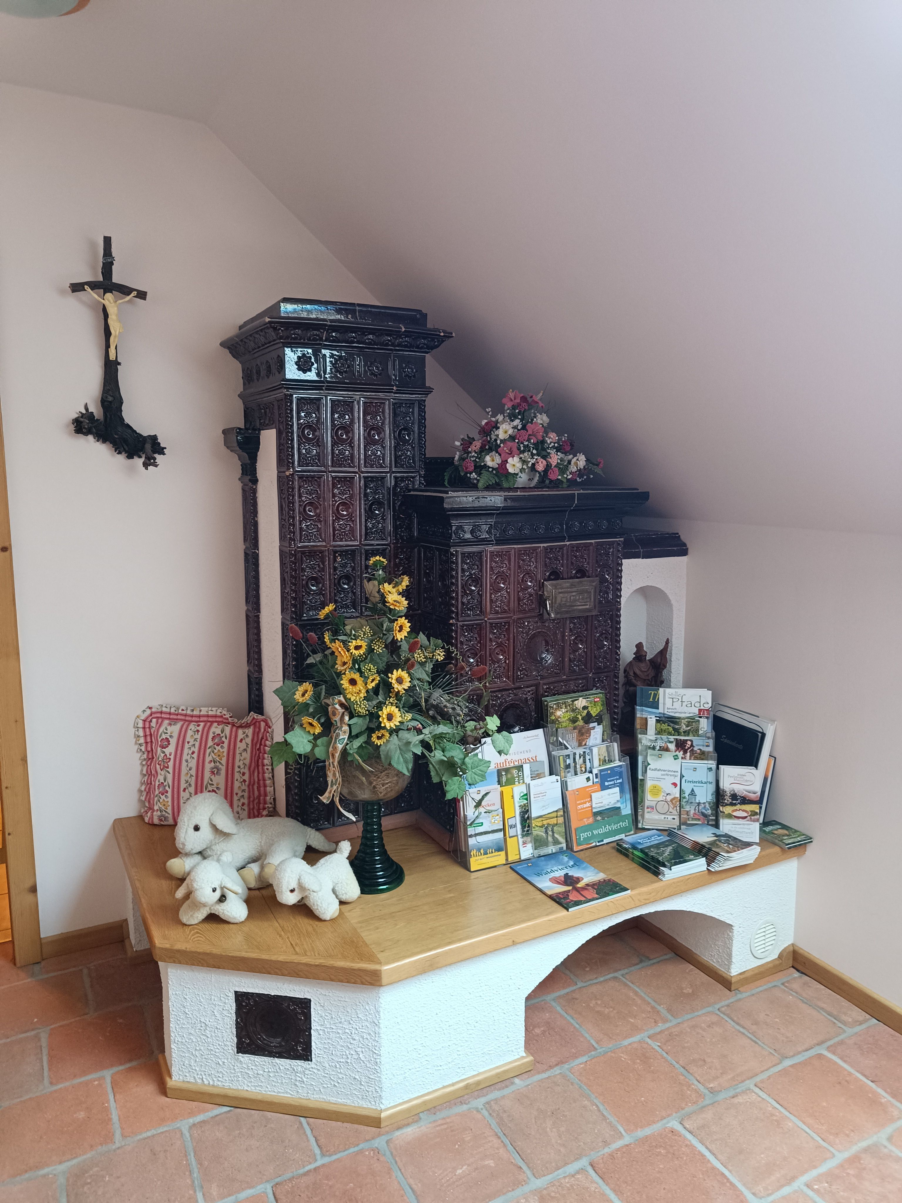 Ein traditioneller Kachelofen in einem Raum mit Broschüren, Stofftieren und Blumen dekoriert.