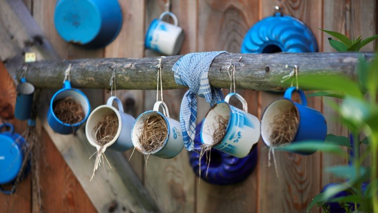 Blaue Emaille-Tassen mit Stroh hängen an einem Holzbalken vor einer Holzwand.