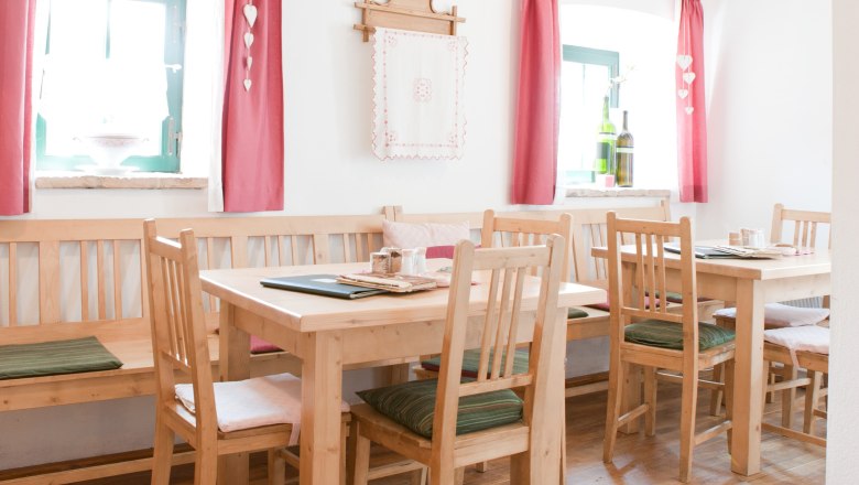 Gemütlicher Gastraum mit Holzmöbeln, roten Vorhängen und Dekoration.