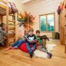 Children in a wooden room with bunk beds, reading a book and holding cuddly toys.