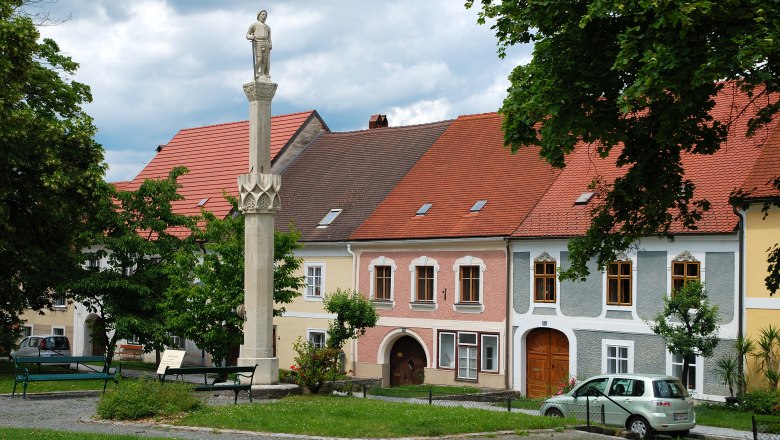 Statue auf einer Säule vor bunten Häusern in Drosendorf.