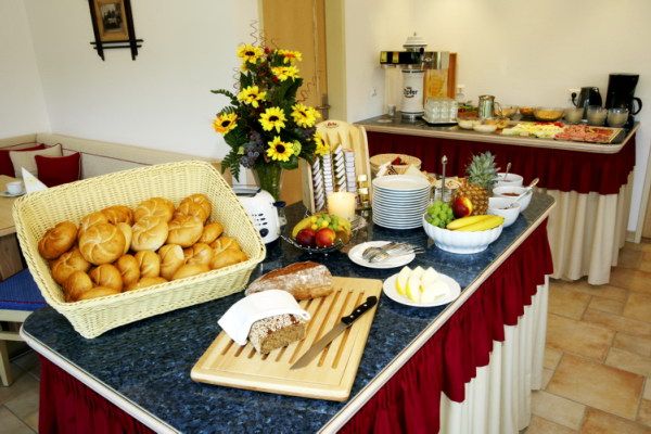 Frühstücksbuffet mit Brötchen, Obst und Blumen.