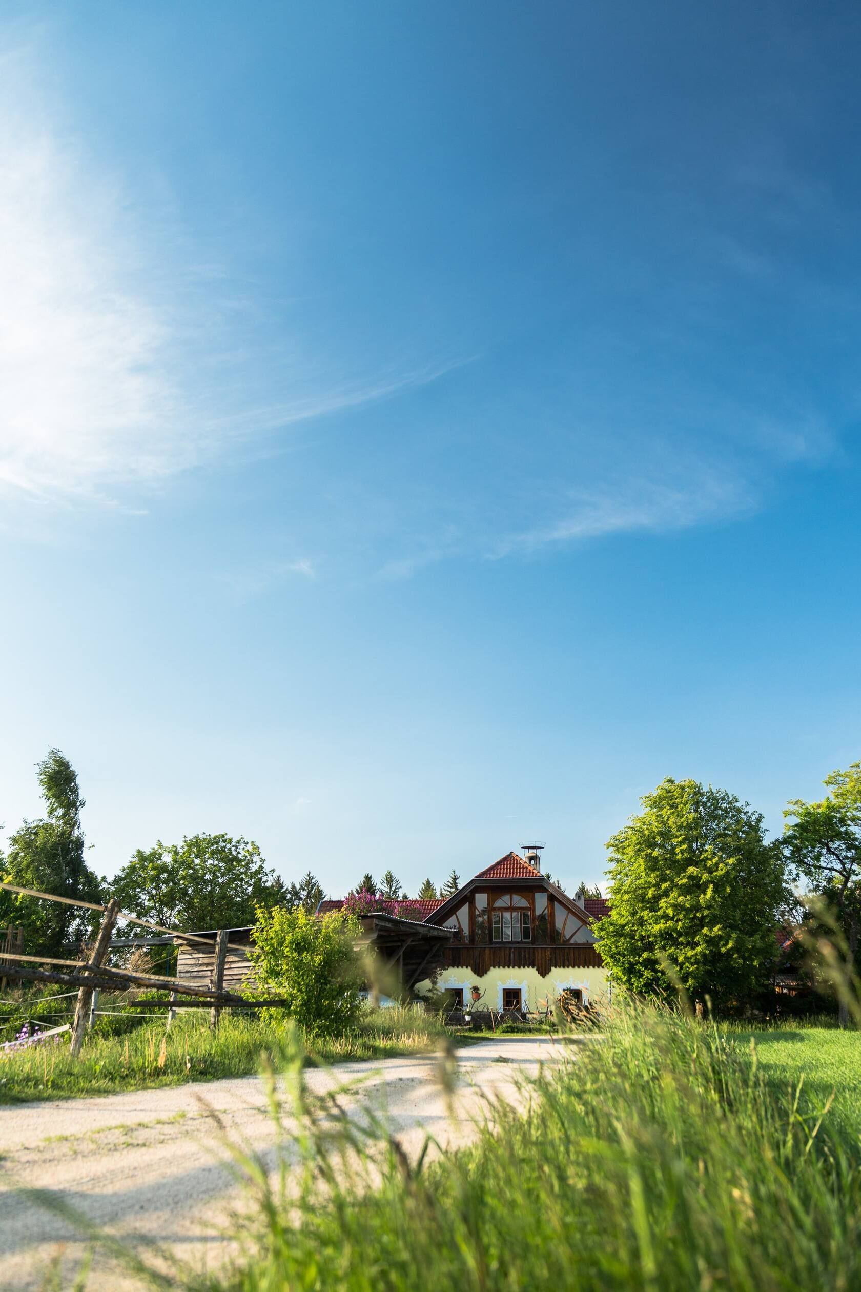 Ländliches Haus mit rotem Dach, umgeben von Bäumen und Wiese unter blauem Himmel.