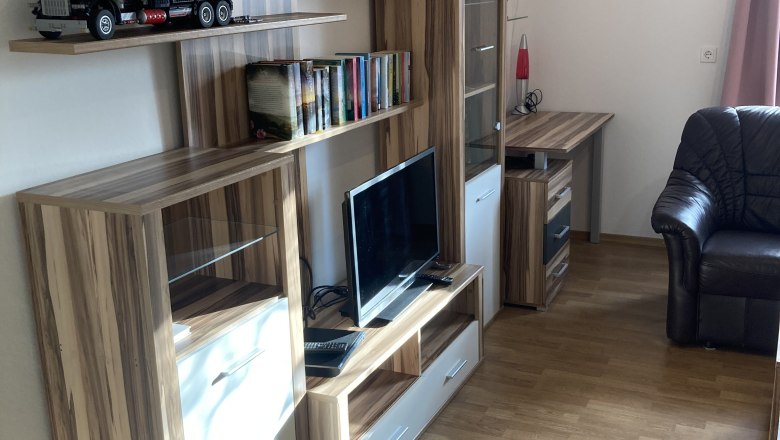 Wohnzimmer mit Holzwohnwand, Fernseher, Bücherregal und Modellauto.