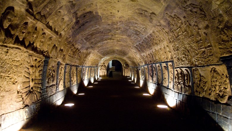 Ein beleuchteter, mit Reliefs verzierter Tunnel in einem historischen Keller.