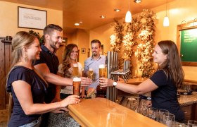 Gruppe von Menschen in einer Bar, die Biergläser anstoßen.