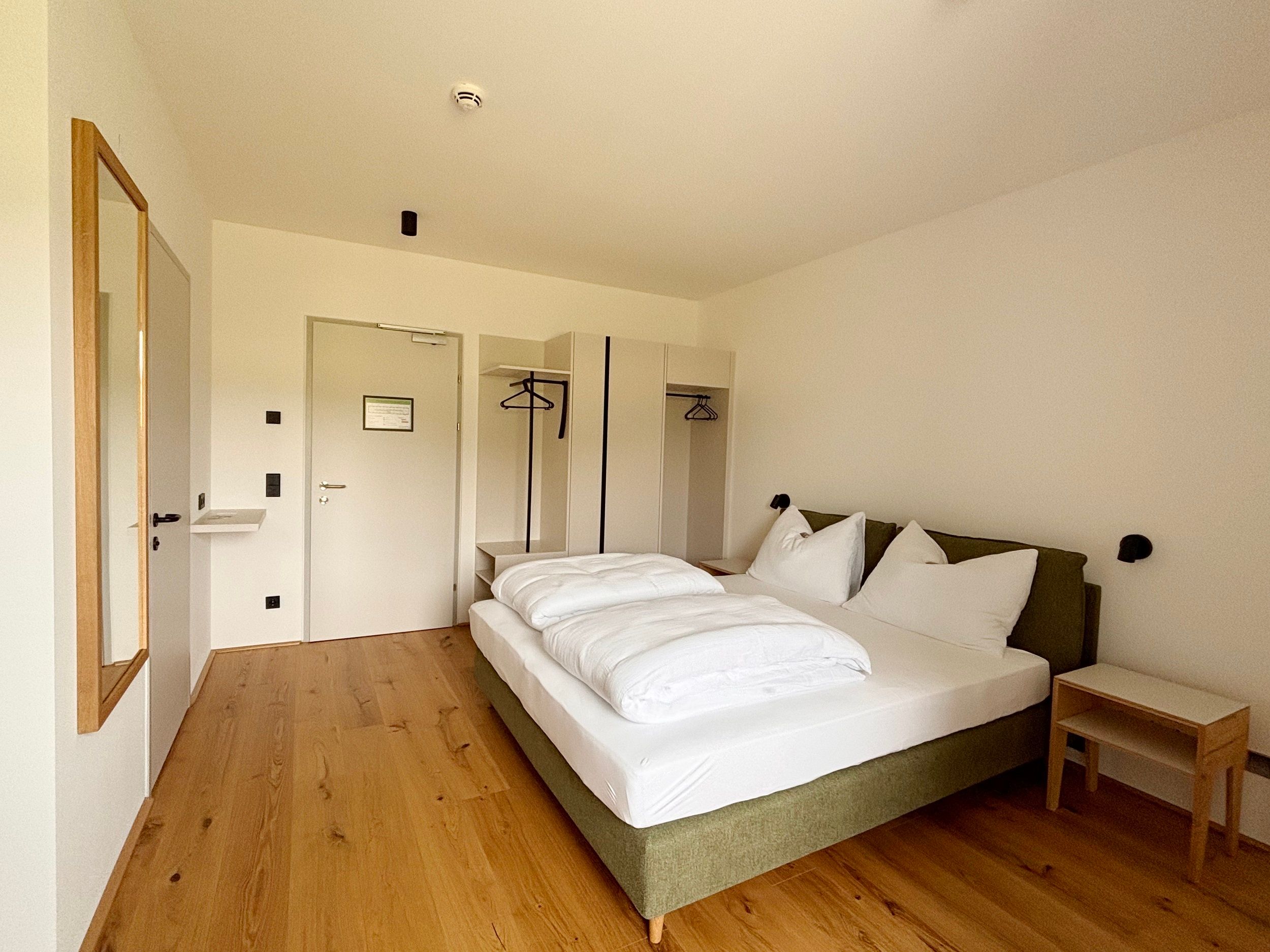 Ein modernes Doppelzimmer mit einem großen Bett, Holzboden und einem offenen Kleiderschrank.