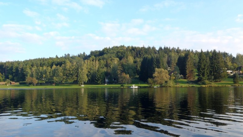 Blick auf den Stausee Thurnberg mit bewaldetem Ufer und klarem Himmel.