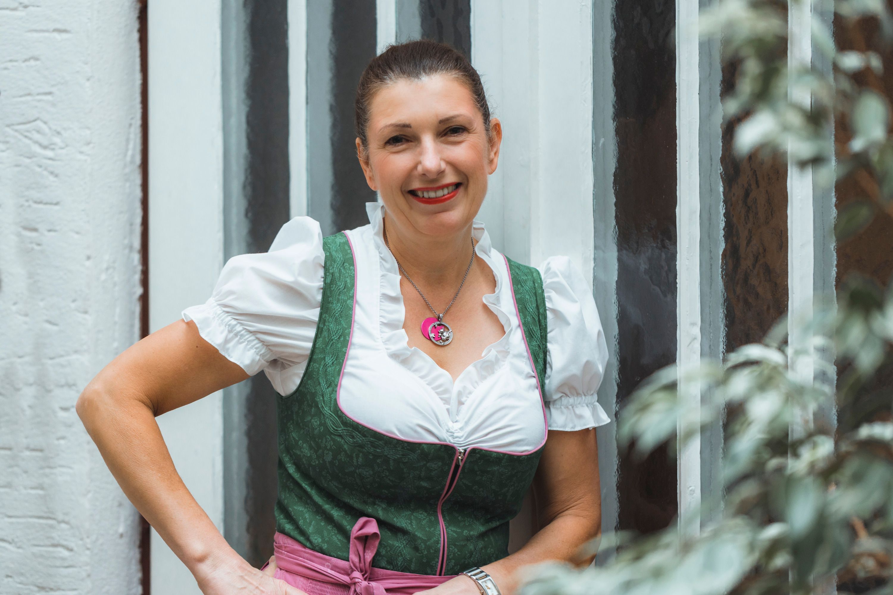 Frau in traditioneller Tracht vor einer Wand mit Glasfenstern.