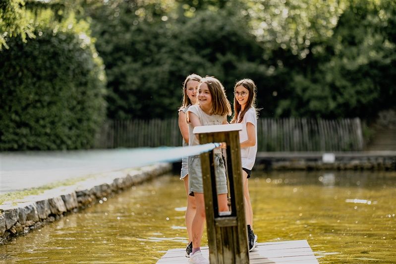 Drei Mädchen stehen auf einem Steg über einem Teich in einem Garten.