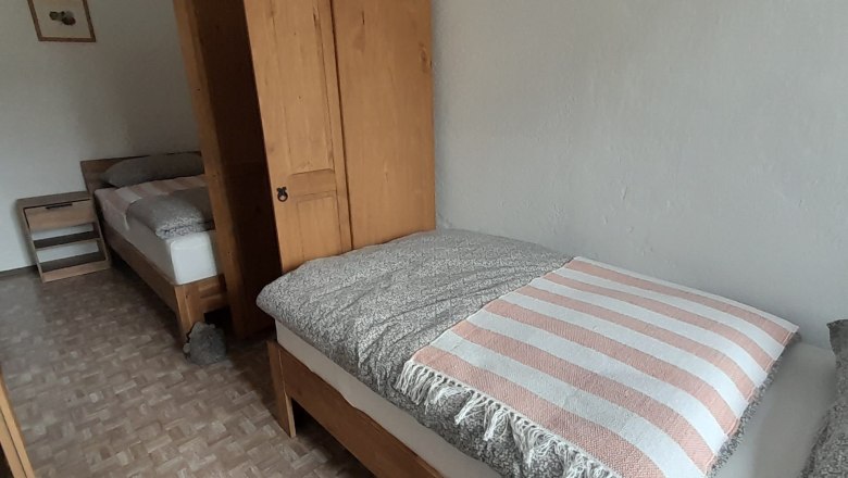 Schlafzimmer mit zwei Einzelbetten, Holzmöbeln und einem Nachttisch.