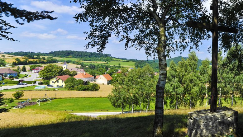 Blick auf eine ländliche Gemeinde mit Kirche und Häusern, umgeben von Feldern und Bäumen.