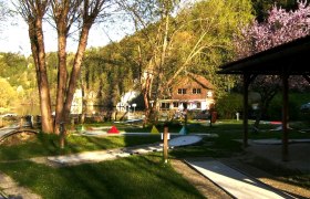 Miniaturgolfplatz mit Bäumen und einem Gebäude im Hintergrund.