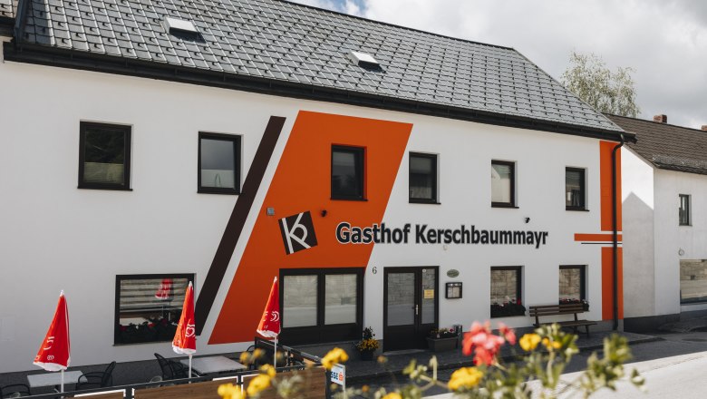 Außenansicht des Gasthofs Kerschbaummayr mit oranger Fassade und roten Sonnenschirmen.