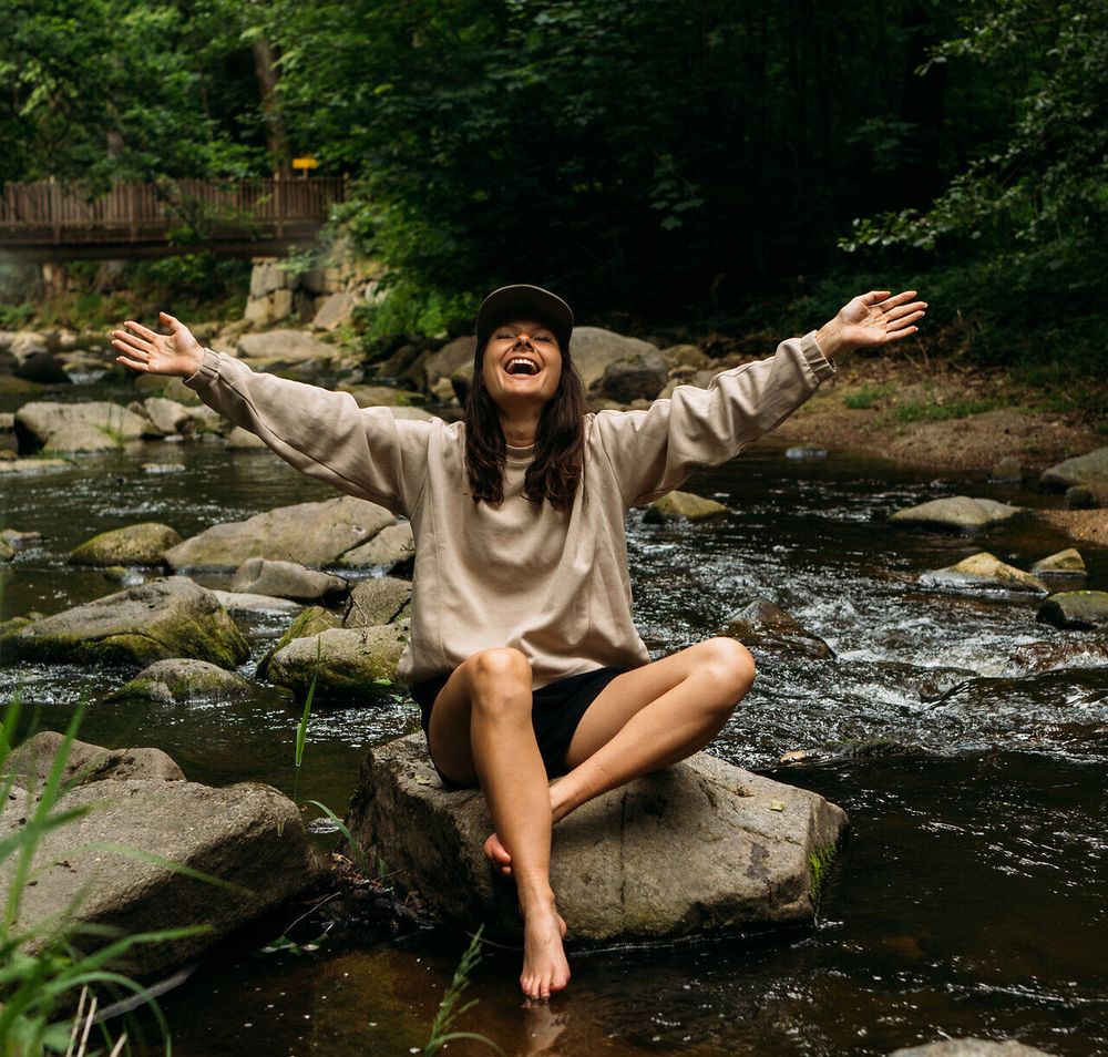 Eine Frau sitzt auf einem Felsen in einem Bach im Gabrielental, umgeben von üppigem Grün, im Waldviertel.