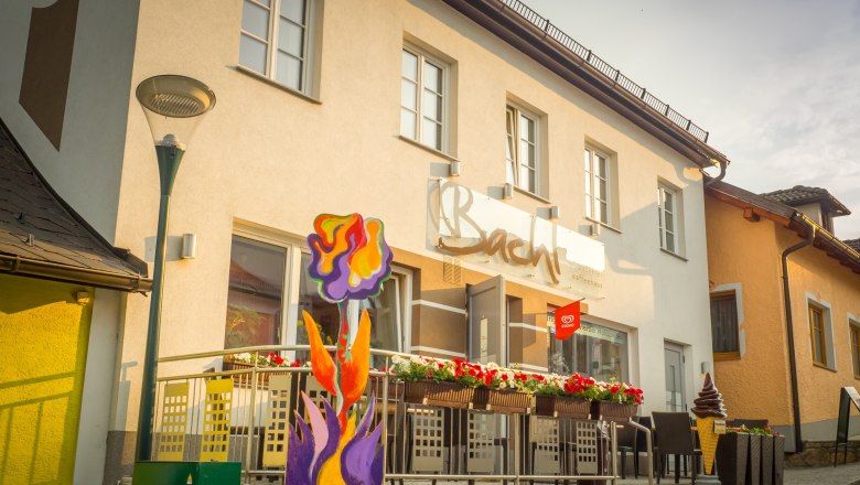 Außenansicht eines Cafés mit Terrasse und bunter Blumendekoration.
