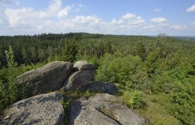 Felsen und Waldlandschaft unter blauem Himmel mit Wolken.