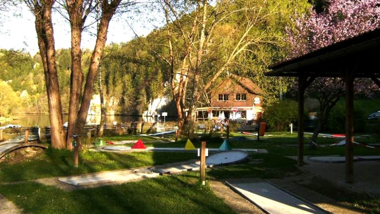 Miniaturgolfplatz mit B&auml;umen und einem Geb&auml;ude im Hintergrund.