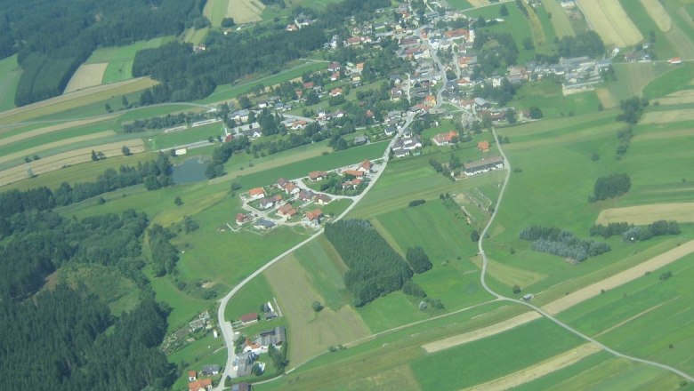 Luftaufnahme einer ländlichen Ortschaft mit Feldern und Wäldern.