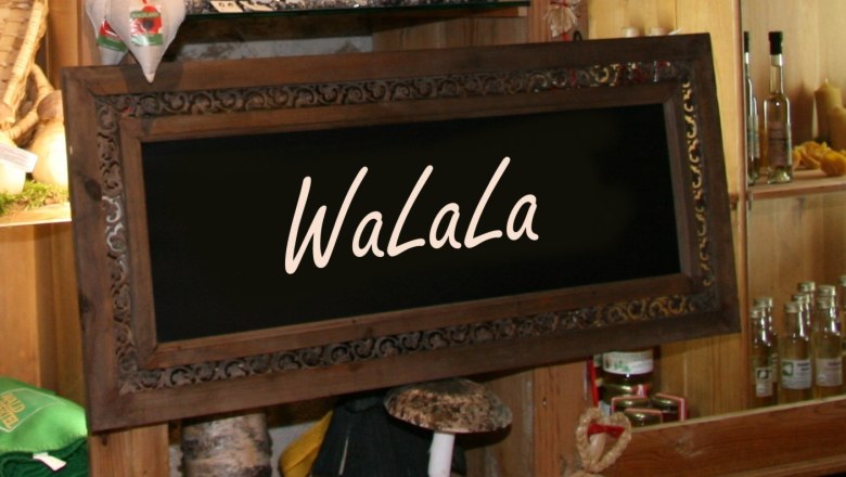 Ein dekoratives Holzschild mit der Aufschrift 'WaLaLa' in einem rustikalen Laden mit Regalen voller Produkte.