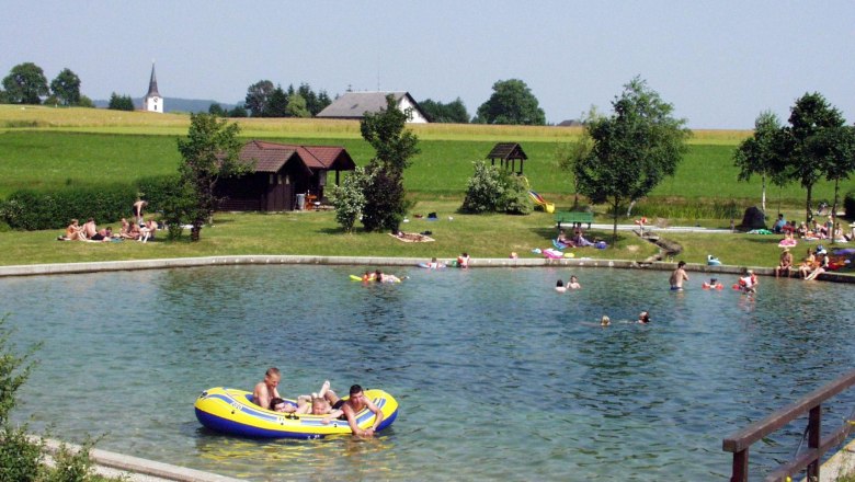 People bathing in a pond with surrounding meadow and trees.