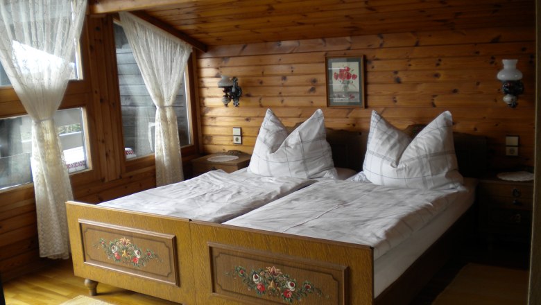 Gemütliches Schlafzimmer mit Holzwänden, Doppelbett und Spitzengardinen.