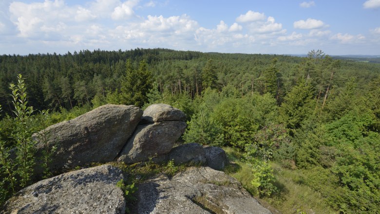 Felsen und Waldlandschaft unter blauem Himmel mit Wolken.