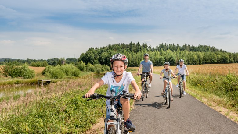 Familie fährt auf einem Radweg durch eine ländliche Landschaft.
