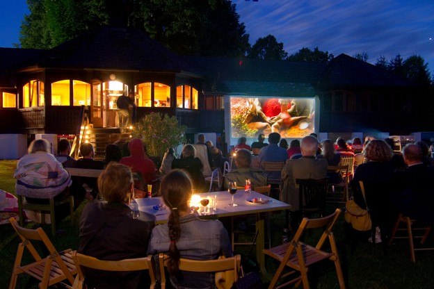 Menschen schauen im Freien einen Film auf einer Leinwand an.