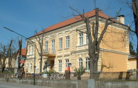 Gelbes Gebäude mit rotem Dach und kahlen Bäumen davor.