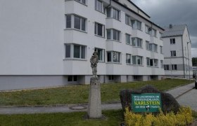 Ein modernes, weißes Gebäude mit mehreren Stockwerken und einem Schild mit der Aufschrift 'Willkommen im Horologenland Karlstein an der Thaya'.