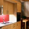 Moderne Küche mit Holzschränken, roter Rückwand, Mikrowelle und Esstisch im Hintergrund.
