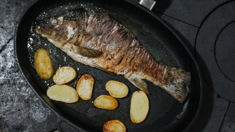Ein gebratener Karpfen mit Kartoffelscheiben in einer Pfanne.