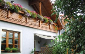 Ein Gästehaus mit Holzbalkon und blühenden Blumen, umgeben von grünen Pflanzen.