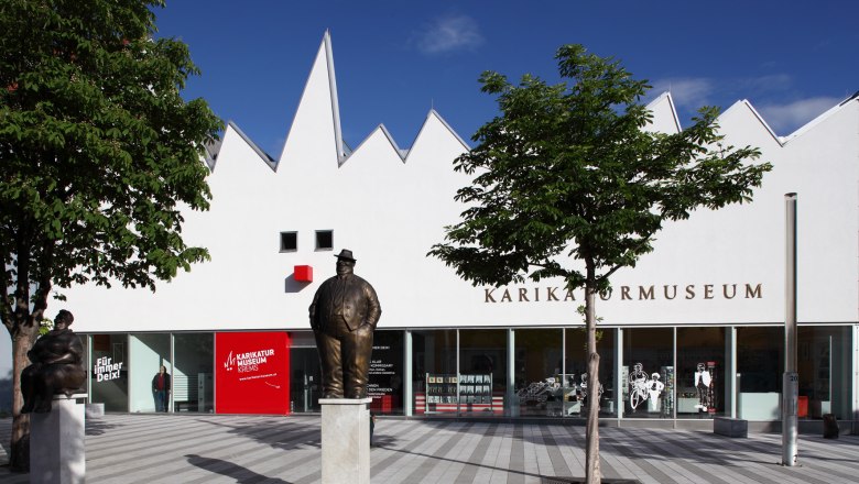 Au&szlig;enansicht des Karikaturmuseums Krems mit Statuen und B&auml;umen.