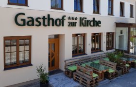 Fassade eines Gasthofs mit Holzpalettenmöbeln vor dem Eingang.