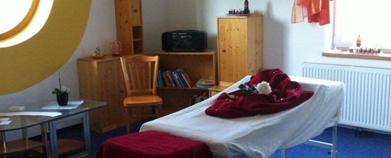 A cozy massage room with massage table, wooden shelves and a large round window.